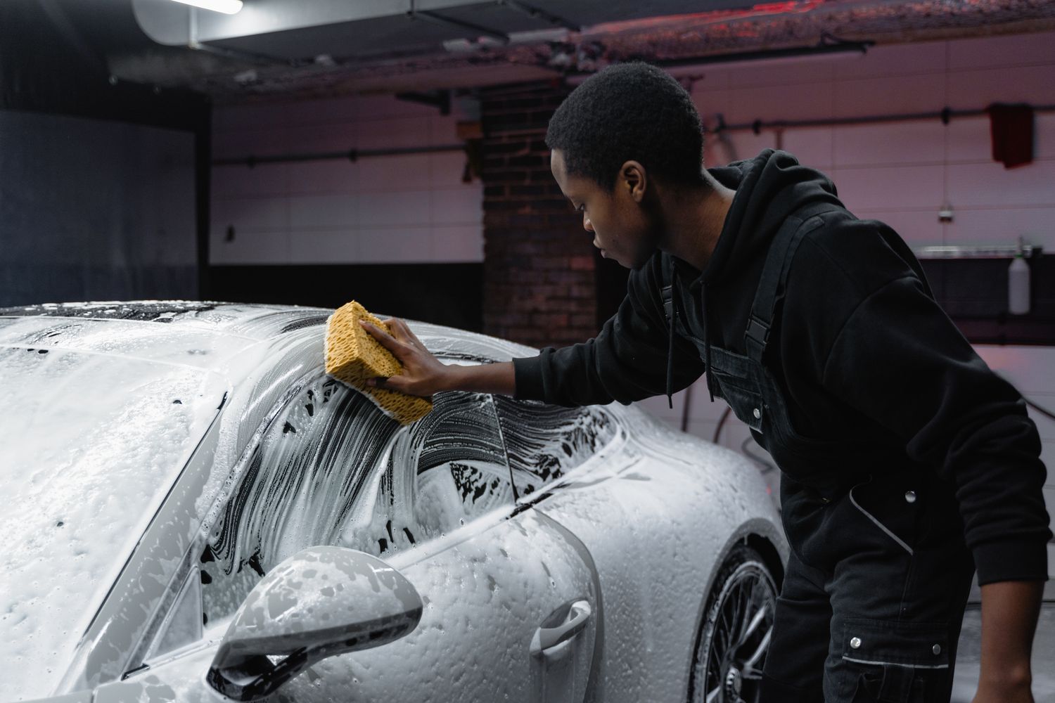 A detailer hand-washing a car in a driveway during a mobile detailing visit