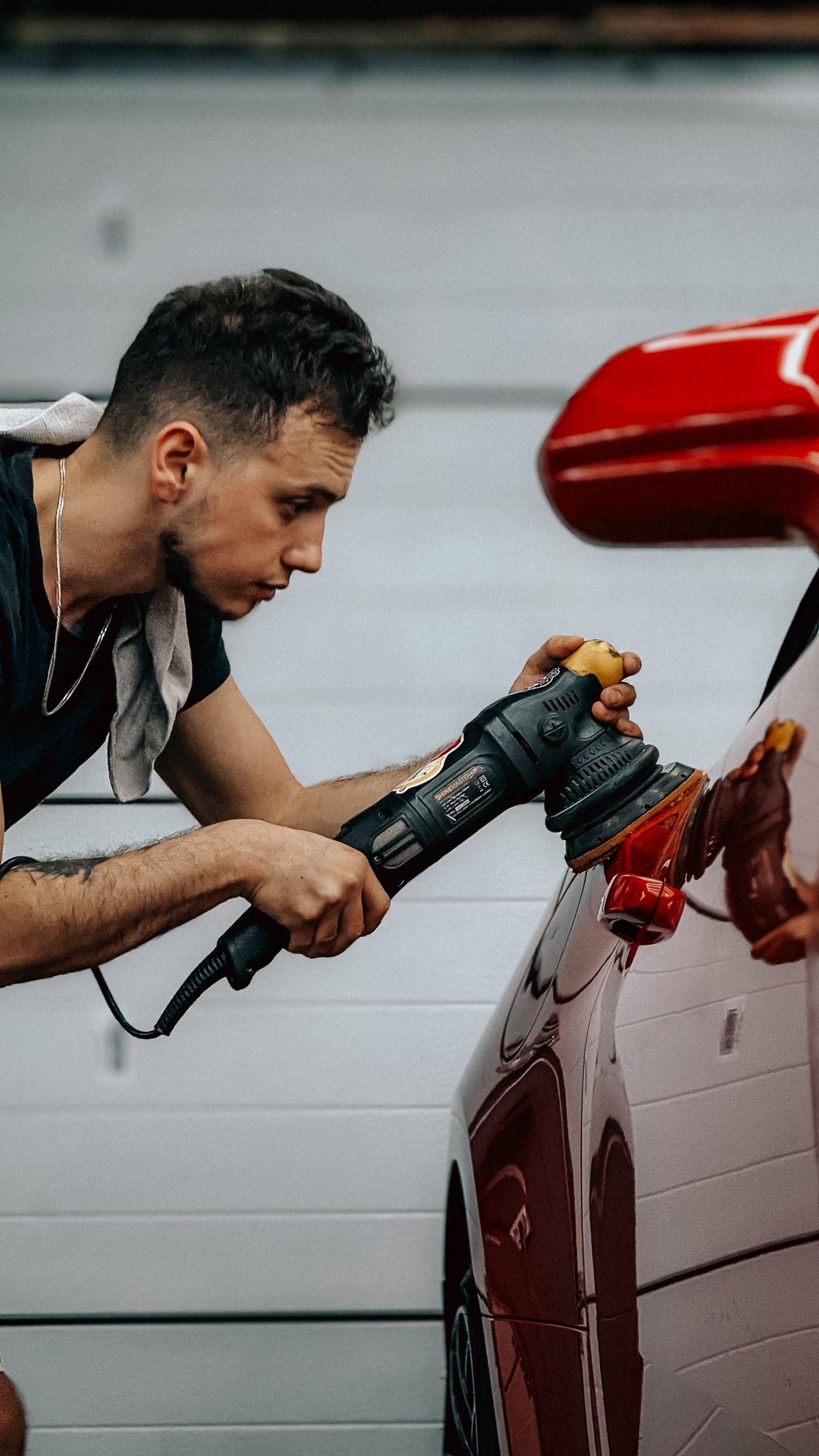 A detailer machine-polishing a car panel to refine the clear coat and restore gloss